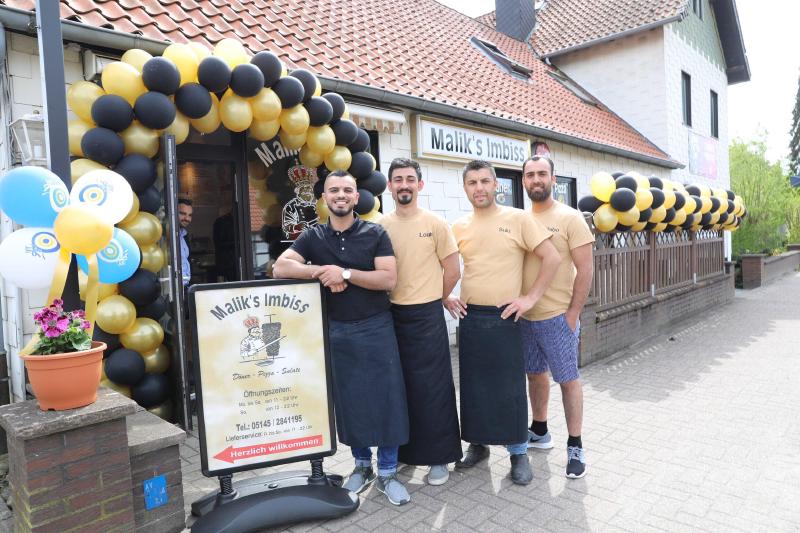 Das Team in Schürzen vor dem Eingang von Malik’s Imbiss, geschmückt mit Luftballons in Gold und Schwarz